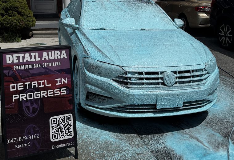 Volkswagen Jetta covered in wash foam beside a Detail Aura sign